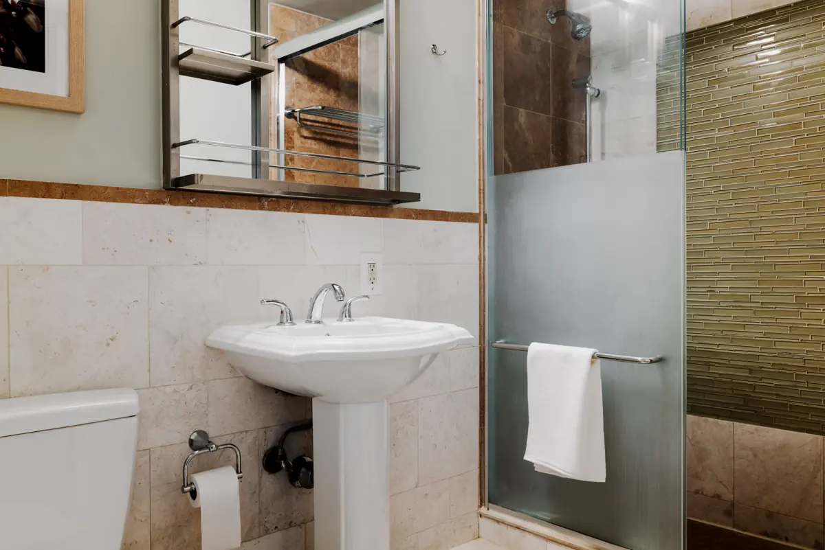 Bathroom with a white pedestal sink, toilet and a frosted-glass shower door with a towel.