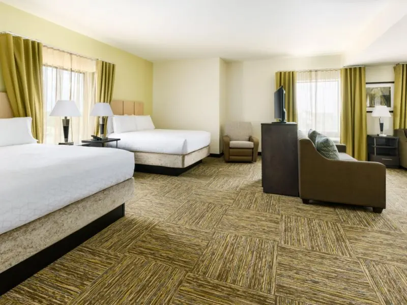 Guest room with two beds, a sofa, a desk with television and windows with gold curtains.