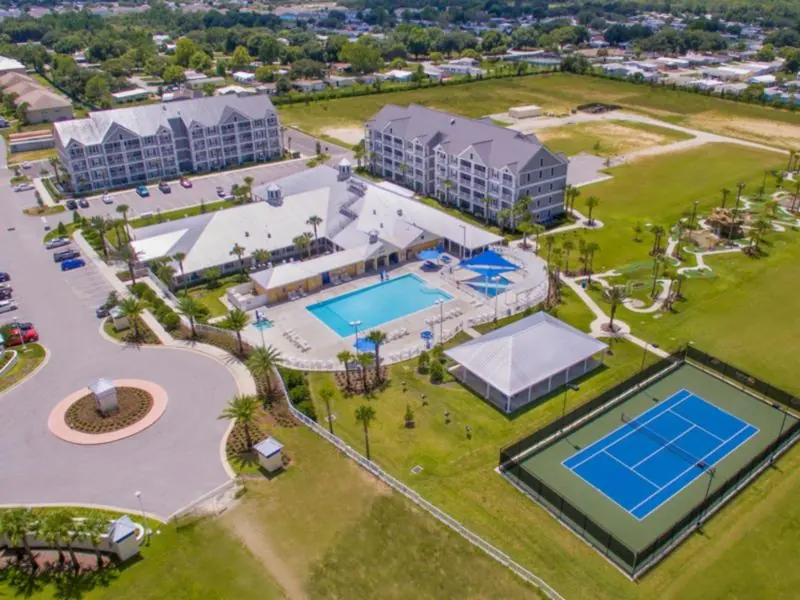 Aerial view of a resort with a pool, a tennis court and several buildings.