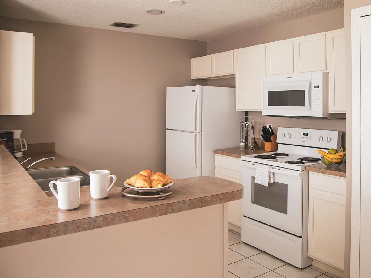 Similar room (illustrative): kitchen with white cabinets, a white refrigerator, electric stove and microwave, and a counter with two mugs and a plate of croissants.