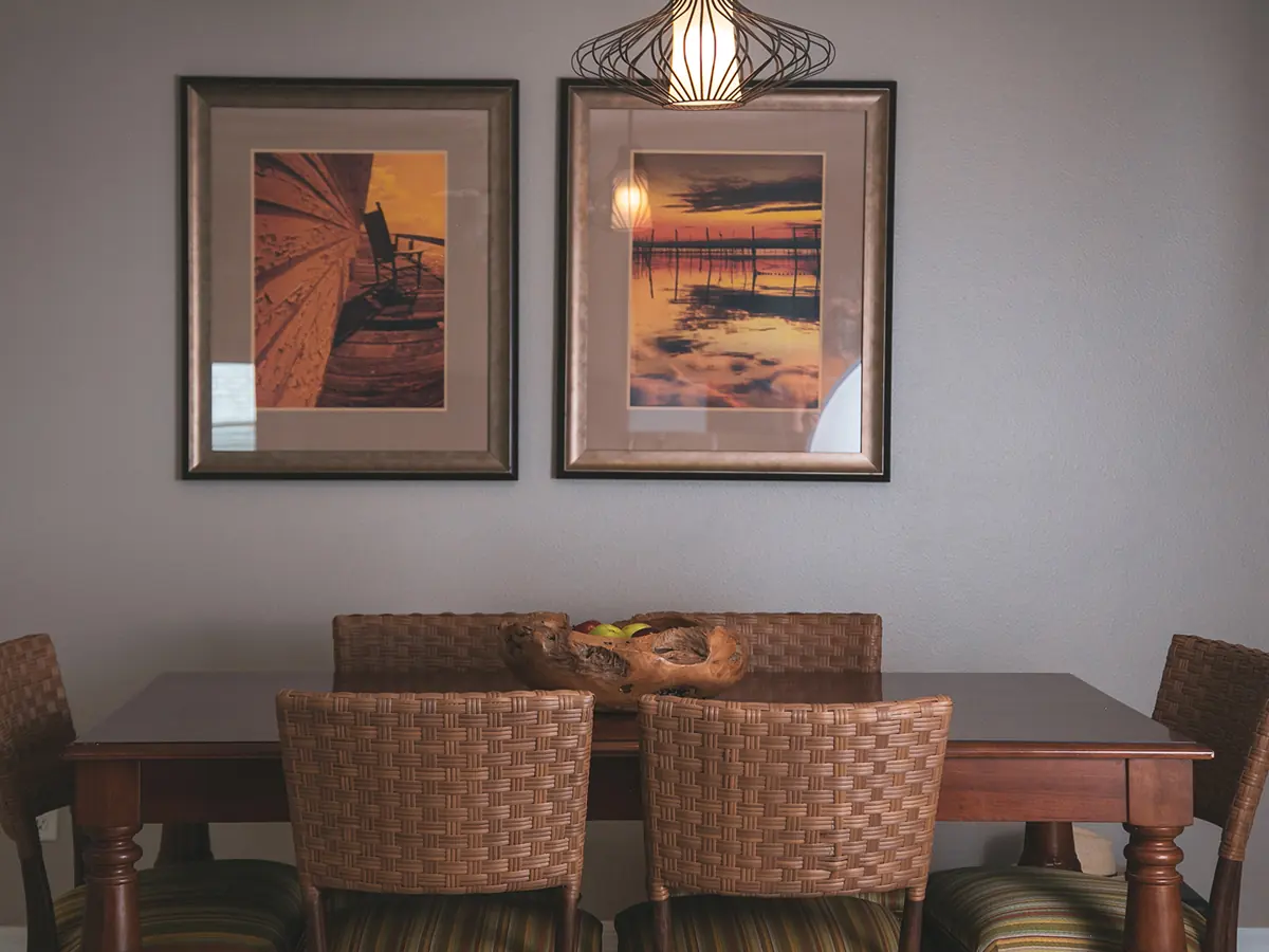 Similar room (illustrative): dining table with woven-seat chairs and two framed sunset pictures on a gray wall.