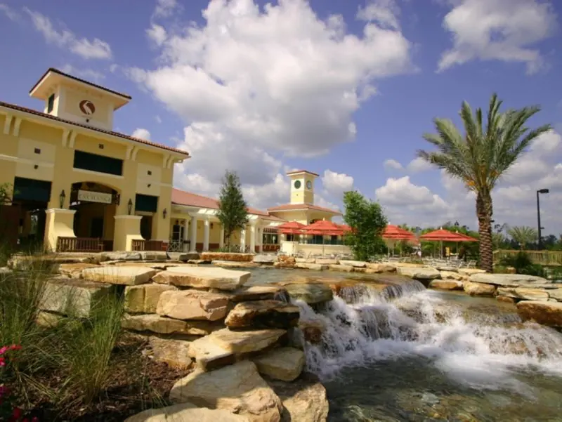 Rock waterfall feature with palm trees in front of a yellow resort building.