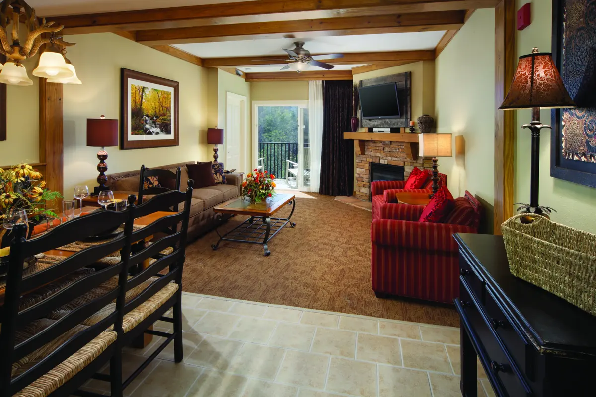 Similar room (illustrative): living area with a dining table in the foreground, a fireplace, red armchairs, a TV and framed autumn pictures.