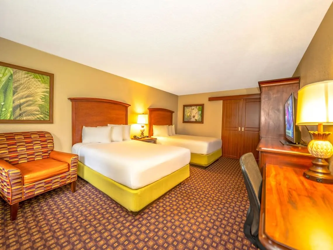Hotel room with two beds with white linens, an armchair, a television on a wooden desk and a wardrobe.