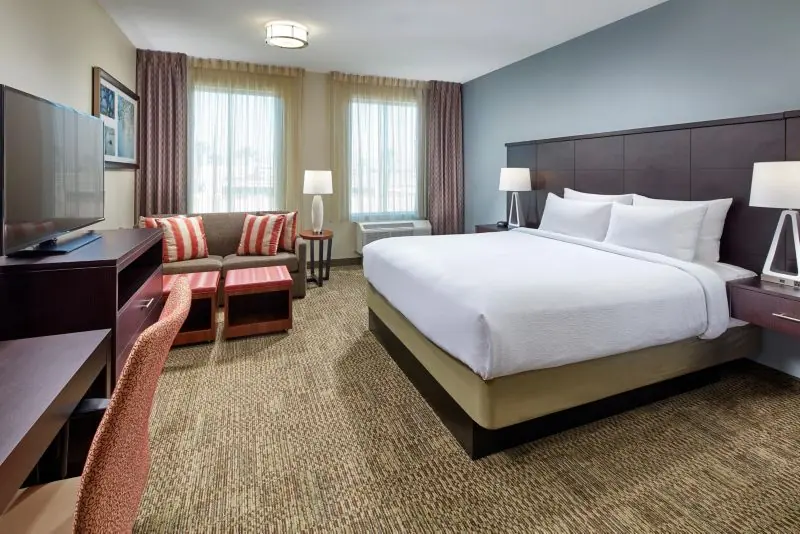 Guest room with a king bed with white bedding, a seating area with a sofa and striped pillows, a desk and a television.
