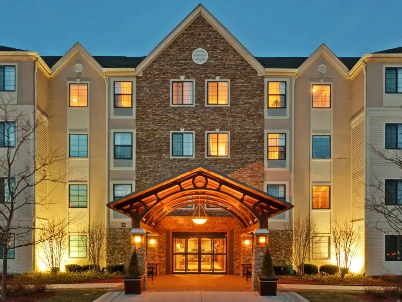 Hotel entrance with a covered canopy, lit windows and a stone and brick facade.