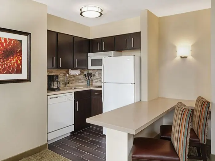 Similar room (illustrative): kitchen with white refrigerator, dishwasher and microwave, dark cabinets, and a breakfast bar with two striped stools.